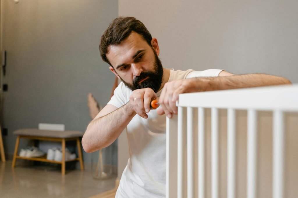 A father attentively assembles a white baby crib in a cozy modern room.